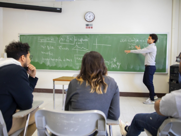 Classroom with instructor pointing at chalkboard with writing