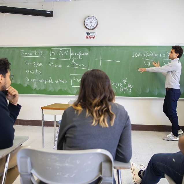 Classroom with instructor pointing at chalkboard with writing